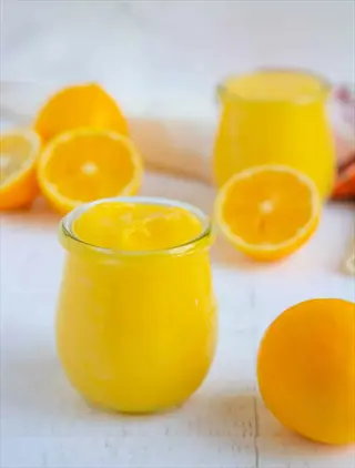 citrus curd jar with fresh oranges and a glass of juice on a white table