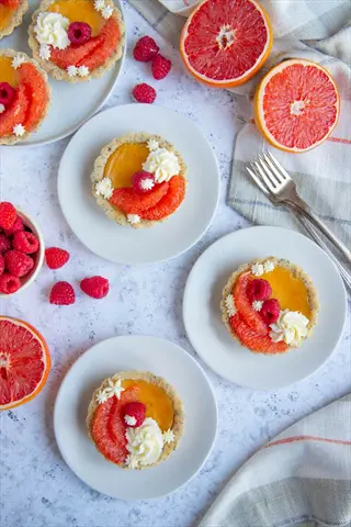 mini citrus tarts with raspberries and rio red grapefruit slices on white plates