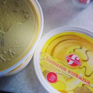 open tub of ice cream banana beside a labeled banana susana lid on a metal counter
