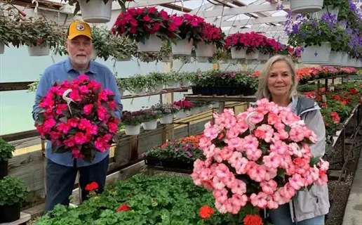 owners holding hanging flower baskets in an independent plant nursery greenhouse