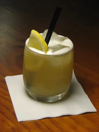 whiskey sour cocktail with lemon garnish and straw on a white napkin