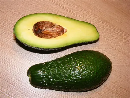 zutano avocado fruit sliced open with pit beside whole green avocado on wooden surface